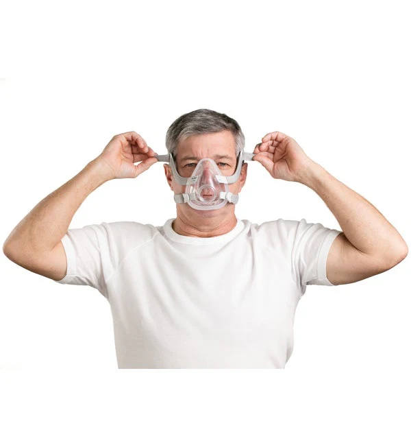 Man fitting ResMed AirFit F20 mask with both hands, adjusting headgear straps, front view