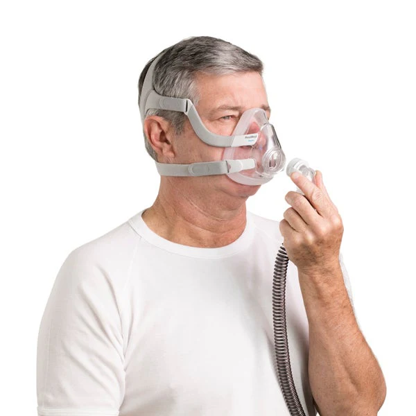 Man wearing ResMed AirFit F20 mask, holding the quick-release elbow connector near the tubing
